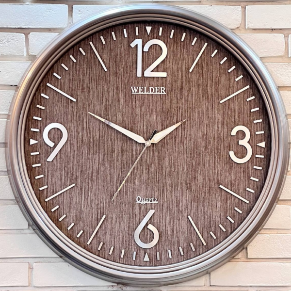 ساعت دیواری ولدر Welder مدل 7010، ساعت دیواری سایز 70 با عقرب های متفاوت، دارای رنگ بندی، شماره برجسته مولتی با فونت لاتین، دارای موتور درجه یک میتسو، رنگ طوسی نقره ای