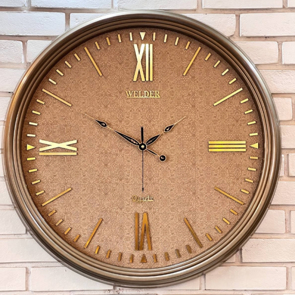ساعت دیواری ولدر Welder مدل 7015، ساعت دیواری سایز 70 با صفحه کاغذ دیواری ترک، دارای رنگ بندی، شماره برجسته مولتی با فونت رومی، دارای موتور درجه یک میتسو، رنگ تیتانیوم طلایی